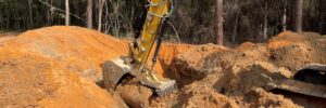 An excavator clearing land in a forested area.