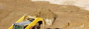 A backhoe lifts up dirt in a land leveling effort near a home