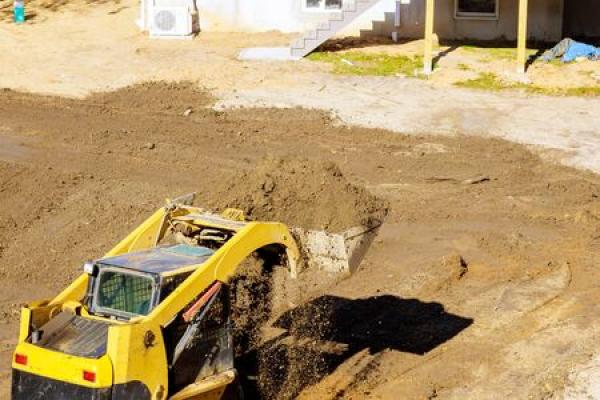 A backhoe lifts up dirt in a land leveling effort near a home